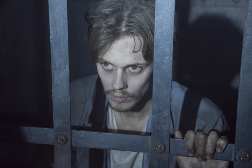 Bill Skarsgard kneels next to his jail cell bars