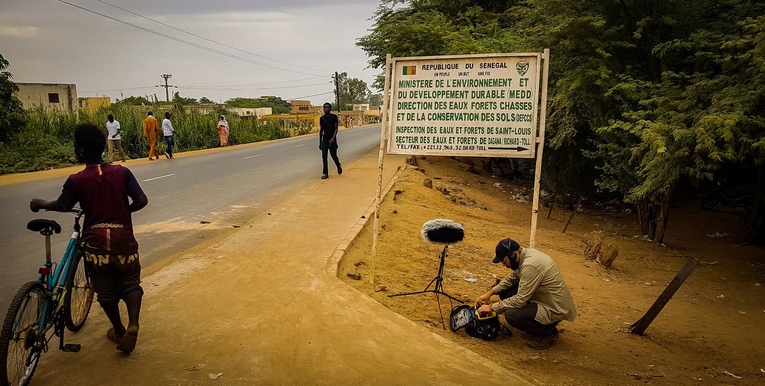 George Vlad records from the side of a town street where pedestrians walk and bike nearby.