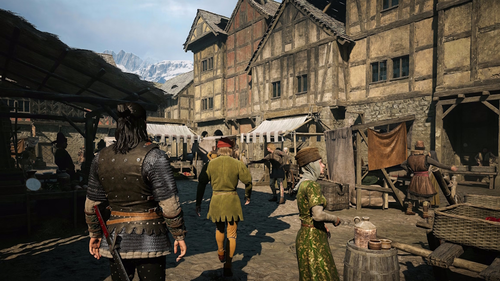 Coen walks through a busy medieval market town in Vale Sangora, with snow-capped mountains in the distance